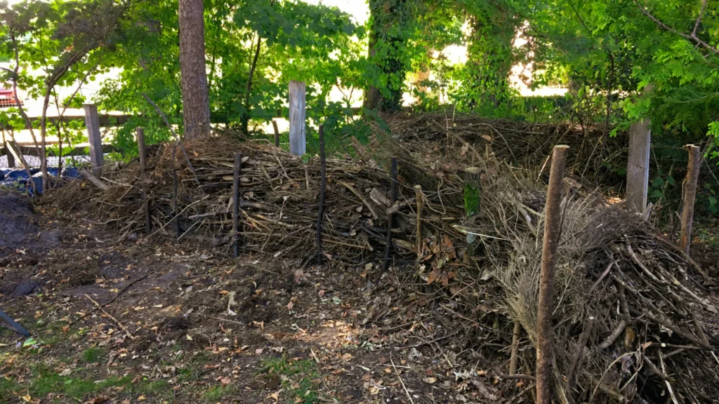 Das Bild zeigt eine Totholz- oder Schichtholzhecke in einem schattigen Garten