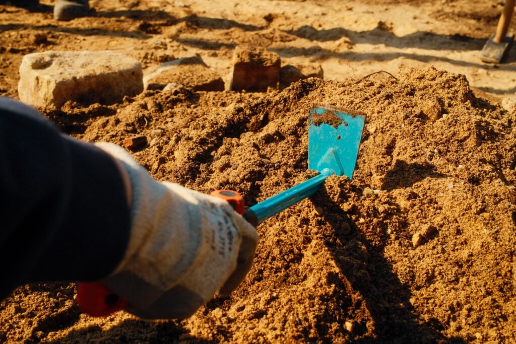 Eine Hand im Gartenhandschuh arbeitet mit der Pflanzhacke